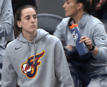 a woman holding a gatorade bottle while wearing a gray nike hoodie