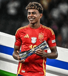 a soccer player in a red adidas jersey holds a trophy