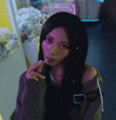 a woman with long black hair is eating a lollipop in front of a neon sign