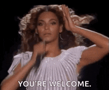 a woman in a white dress is holding a microphone in her hand and saying `` you 're welcome '' .