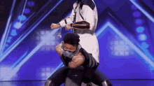a man is carrying another man on his shoulders on a stage with a purple background