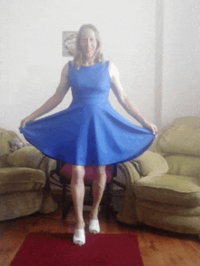 a woman in a blue dress is standing in front of a couch