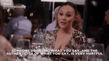 a woman in a leopard print top is sitting at a table with wine glasses and says someone doubting what you say