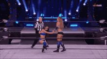 two women are wrestling in a ring with a referee in the background .