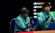 two people are clapping in front of a screen that says maschia
