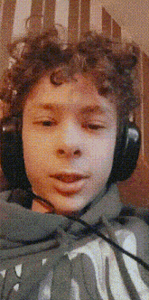 a young boy with curly hair is wearing headphones and a microphone around his neck .