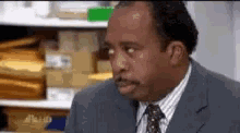 a man in a suit and tie is sitting in front of a shelf filled with envelopes .