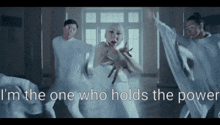 a woman in a white dress is surrounded by other people with the words " i 'm the one who holds the power " above her