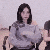 a woman in a gray sweater is sitting in a chair and holding a remote control .