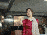 a woman in a red dress with a scarf around her neck stands in a room