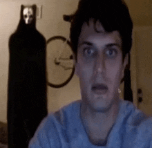 a man in a blue shirt is looking at the camera with a ghost in the background
