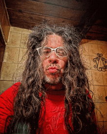 a man with long hair wearing glasses and a red shirt