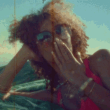 a woman wearing sunglasses and a red top is covering her mouth