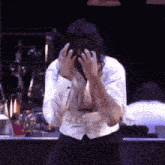 a man wearing a white shirt and black pants is covering his face with his hands