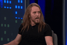 a man with long hair is sitting in front of a sign that says open your buttcheeks