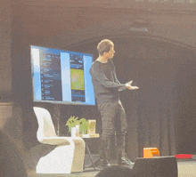 a man stands on a stage in front of a screen that says ' a ' on the top left
