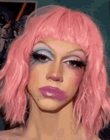 a woman wearing a pink wig and purple makeup is making a funny face .