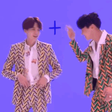two men in suits are standing next to each other in front of a blue background and a plus sign .