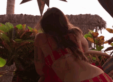 a woman in a red bikini stands in front of a thatched roof