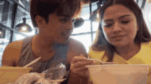 a man and a woman are sitting at a table eating from bowls .