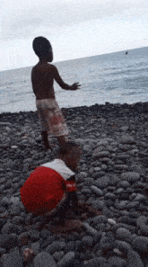 two boys playing on a rocky beach with one wearing a shirt that says ' coca cola '