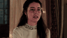 a woman with long hair is wearing a white top and earrings