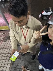 a woman giving a peace sign while a man points at a phone