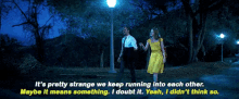 a man and a woman are walking in a park at night and the woman is wearing a yellow dress