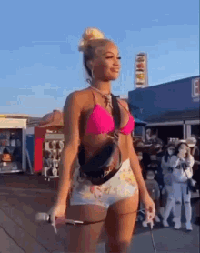 a woman in a pink bikini and shorts is walking down a boardwalk .