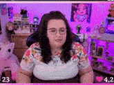 a woman wearing glasses and a floral shirt is sitting in front of a pink wall .