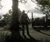 a man in a cowboy hat is standing next to a tree in a field