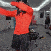 a man wearing a red sweater and black shorts is dancing in a room .