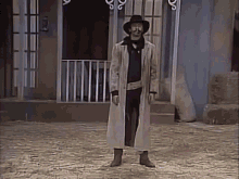 a man wearing a cowboy hat and a long coat stands in front of a building
