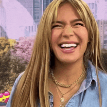 a woman wearing a necklace and a denim shirt is smiling .
