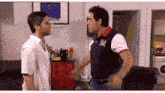 two men are fighting in a living room and one of them is wearing a blue and white polo shirt with the letter r on it