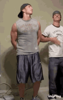 a man in a tank top and shorts is standing next to another man in a hat .
