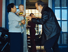 a man in a leather jacket holds a baby while a woman holds a stroller