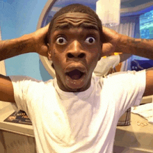 a man in a white shirt is making a surprised face with his hands on his head