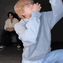 a man in a blue sweatshirt is sitting on the floor with his eyes closed