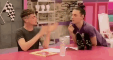 two men are sitting at a table talking to each other .