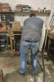 a man in a vest is using a vacuum cleaner in a workshop