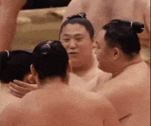 a group of sumo wrestlers are hugging each other in a wrestling ring .