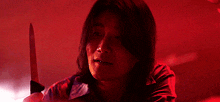 a woman is holding a large knife in her hand in a dark room .