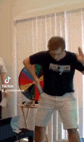 a man in a black shirt and white shorts is dancing in front of a spinning wheel .