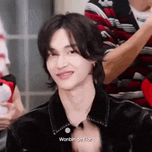 a young man with long black hair is wearing a black jacket and earrings .