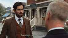 a man in a suit and tie is talking to another man in front of a building that says everything 's aces constable