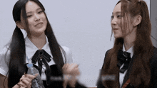 two girls in school uniforms are standing next to each other and smiling . one of the girls is holding a bottle of water .
