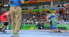 a referee watches two wrestlers in a wrestling match with a scoreboard that says live on it