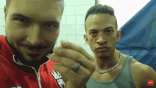 two men are posing for a picture and one has a ring on his finger and the other has a chain around his neck