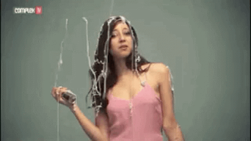 a woman in a pink dress is standing in front of a wall with her hair covered in liquid .
